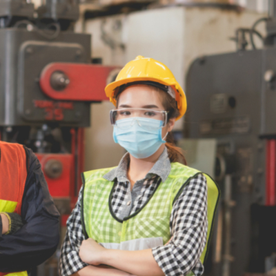Female worker in a manufacturing site wearing a mask and hard hat