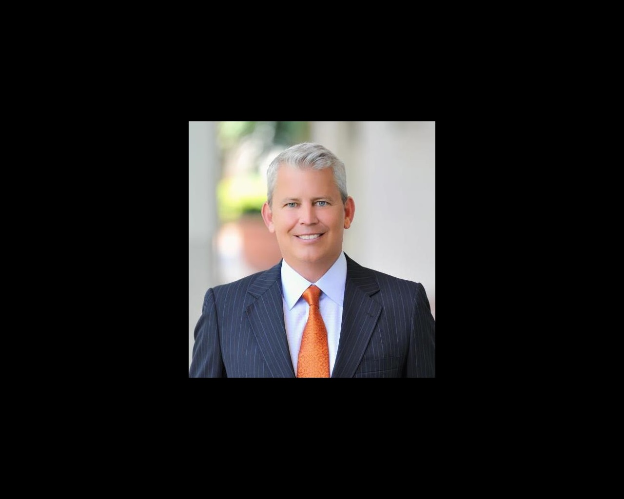 Sean Domnick standing outside wearing a dark grey suit and orange tie.