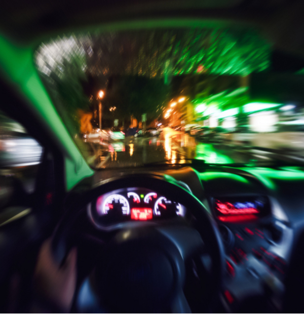 Looking over the steering wheel and through the windshield of a car at night with blurry bright lights.