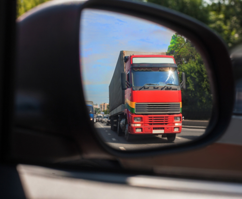 Reflection of red tractor trailer in car side mirror