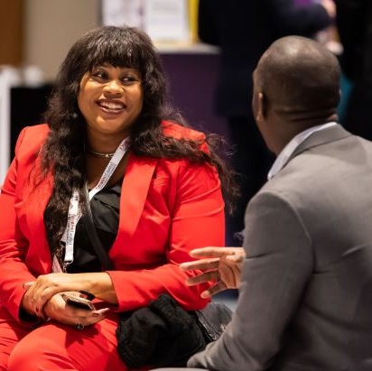 Female attorney in red suit speak with colleague in a grey suit.