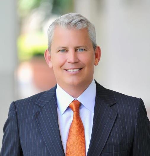 Sean Domnick standing outside wearing a dark grey suit and orange tie.