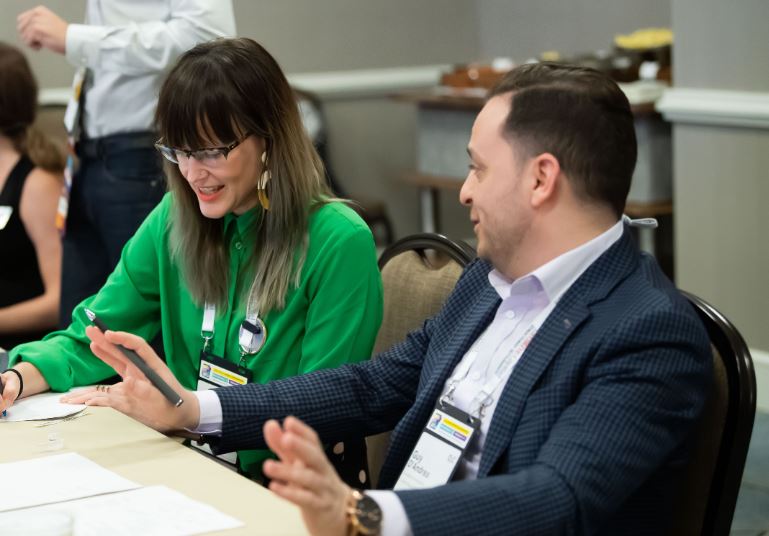 Woman in green shirt and man in blue blazer laughing while talking.