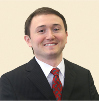 Joshua Basile wearing a dark suit and a red tie.