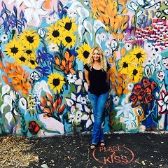 Woman wearing a black shirt and jeans standing in front of flower mural