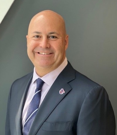 Chris Nace in black suit with pink and blue tie