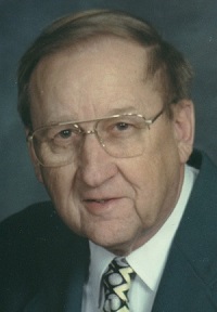 Headshot of an man with glasses and wearing a dark suit and patterned tie.