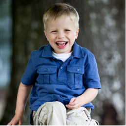 Young blond boy wearing a blue shirt and khaki pants laughing.