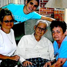 Man in a white button of shirt sitting in a chair, surrounded by 3 other people.