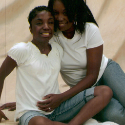 Two woman, wearing white tshirts and jeans sitting on the floor hugging.