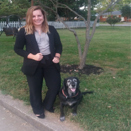 Woman wearing black suit standing on a curb next to a dog