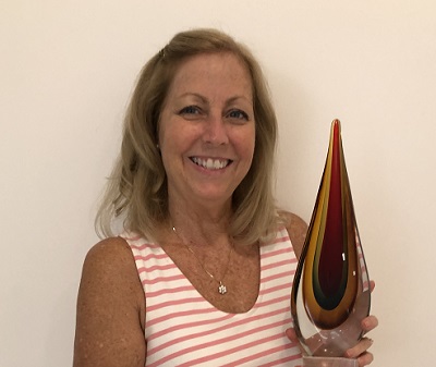 Woman wearing a pink and white striped sundress holding a tear shaped red glass award.