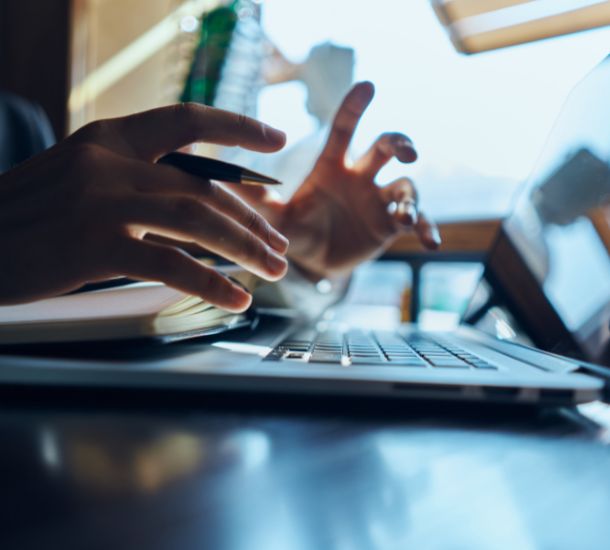 A close up photo of a laptop in use with two hands hovering over the keyboard